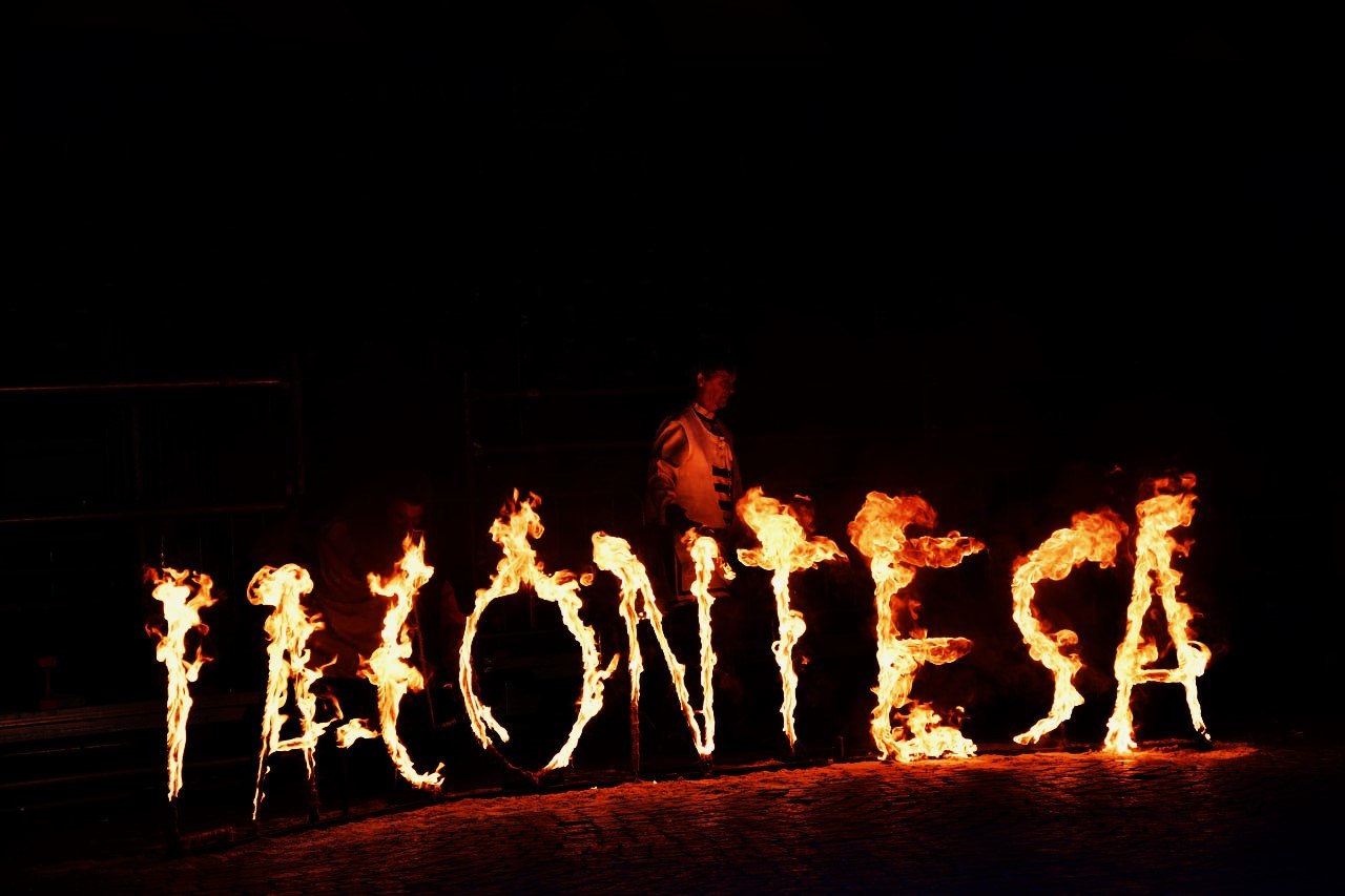 Scritta ‘La Contesa’ realizzata con fuoco durante una rievocazione notturna, con fiamme che formano le lettere davanti a una tribuna.